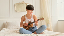 Young Woman Playing On Ukulele Practicing Music Guitar At Home. Learning To Play A Musical Instrument.