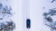 Aerial top view from drone of suv vehicle driving on snowy ice road exploring local landscapes in winter, bird’s eye view of automobile car moving on area surround by beautiful coniferous forest