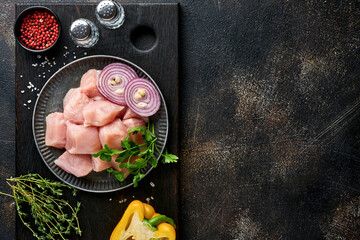 Wall Mural - Raw pieces meat ingredients of chicken on wooden board, spices, herbs and vegetables on dark grey background. Raw ingredients for goulash or shish kebab. Top view. Free copy space.