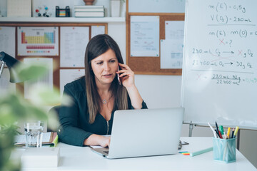Wall Mural - Female professor having break with online class and talking on mobile phone .
Displeased teacher calling somebody on phone and preparing to working from home desk with E-learning students online.