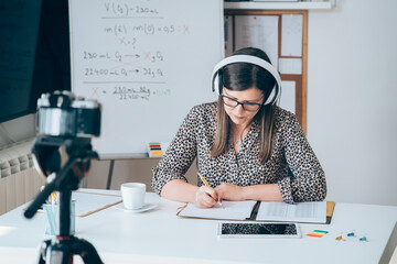 Wall Mural - Teacher recording video tutorial for e-learning class.
Female professor working from home teaching online physic to student studying from home. Woman using camera and headset for live streaming.