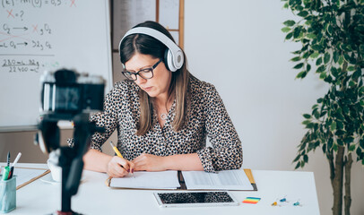 Wall Mural - Teacher recording video tutorial for e-learning class.
Female professor working from home teaching online physic to student studying from home. Woman using camera and headset for live streaming.