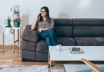Wall Mural - Happy Business Woman Sitting on Sofa and Talking on Mobile Phone
Cheerful smiling businesswoman relaxing on couch in living room at home and calling somebody on smartphone.