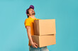 © Valerii Apetroaiei - Young bearded courier delivery man in uniform holding heavy boxes isolated on blue background. Home delivery.