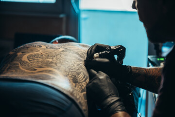 Hands of a tattoo artist wearing black gloves and holding a machine