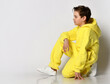 Stylish active guy in a bright yellow neon tracksuit, sitting on one knee and looking to the side on a white background. The concept of comfortable clothing, children's sporty and active lifestyle.