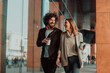 © .shock - two people on a break from work walk in front of a modern company where they work and drink coffee.