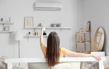 Poster - young woman with air conditioner remote control on sofa at home