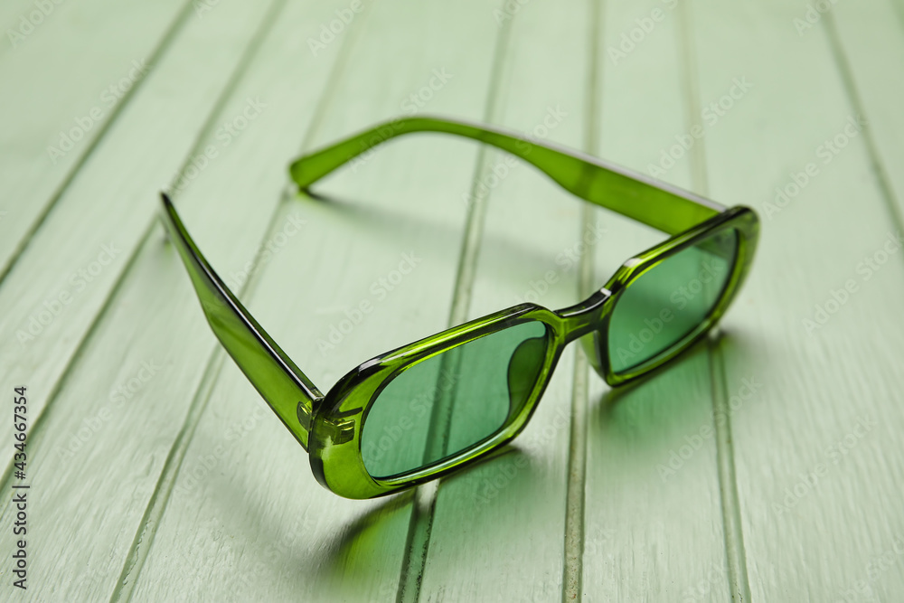 Stylish sunglasses on color wooden background, closeup