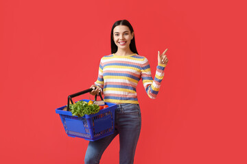 Sticker - Young woman with shopping basket pointing at something on color background