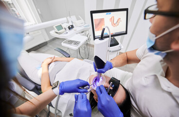 Close up of dentist and assistant using dental intraoral scanner while examining patient teeth in dental office. Specialist in sterile gloves performing intraoral scanning with modern scanning machine