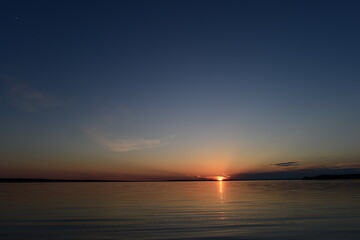 Wall Mural - Sunbeam at sunset from clouds on the horizon above the lake water