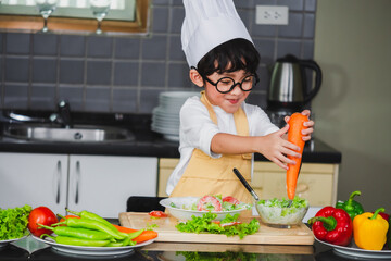 Wall Mural - Asian Boy son cooking salad food holdind wooden spoon with vegetable holding tomatoes and carrots, bell peppers on plate for happy family cook food enjoyment lifestyle kitchen in home