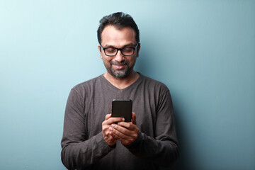 middle aged man of indian origin looking at his mobile phone with a smile