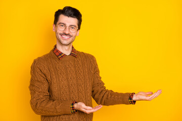 Sticker - Photo of young charming smart man hold hand empty space decide product offer isolated on yellow color background