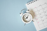 white analog alarm clock on calendar with grunge blue background with copy space, business meeting schedule, travel planning or project milestone and reminder concept