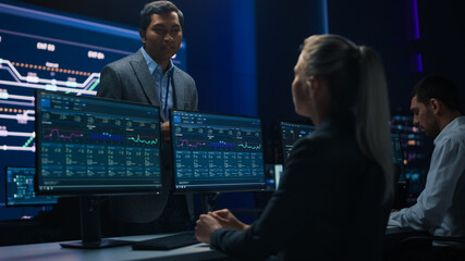 Poster - Confident Female Specialist Works on Computer Talks with Team Leader in Big Infrastructure Control Room. Business Woman Professional Uses Computer Showing Charts, Information. Monitoring Room Teamwork