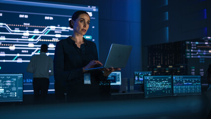 Aufkleber - Beautiful Confident Female Project Manager works on Laptop Standing in Telecommunications System Control Room. In Background Big Screen Showing Infographics of Infrastructure, Charts, System Analysis