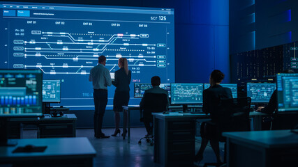 Fototapete - Telecommunications Company System Control and Monitoring Room with Diverse Multicultural Team of Professionals Working on Computers. Big Screen Display Showing Infrastructure Infographics. Back View