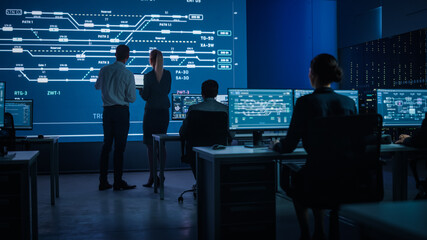 Fototapete - Telecommunications Company System Control and Monitoring Room with Diverse Team of Professionals Working on Personal Computers. Big Screen Display Showing Infrastructure Infographics and Data
