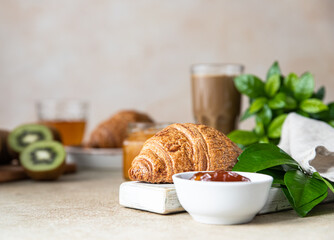 Poster - Breakfast with a cup of coffee, fresh crispy croissant, jam, kiwi and juice, light stone background. Summer breakfast.