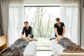 Two masseurs doing a deep back massage to guests with pampering technique. Wellness and leisure time for health care together with forest view in window.