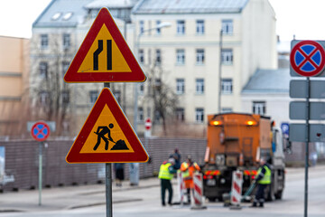 warning signs about street repairs on a blurred background with repair workers, closeup