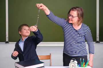 Funny junior boy in school uniform and angry teacher with handcuffs in school class