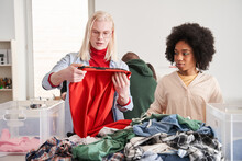 Man Wearing Glasses Examining And Sorting Clothes For Altering With His Colleague