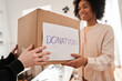 Multiracial woman taking box with second-rate clothing for the recycling and smiling