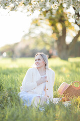 Beautiful young woman in a wicker hat is resting on a picnic in a blooming garden. White flowers. Spring. Happiness.