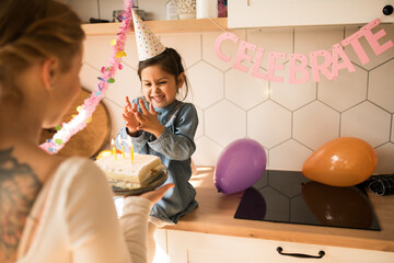 Wall Mural - Mother holding plate with birthday cake near daughter while wishes happy birthday