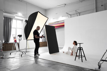 Wall Mural - Fashion photography in a photo studio. Professional male photographer taking pictures of beautiful woman model on camera, backstage