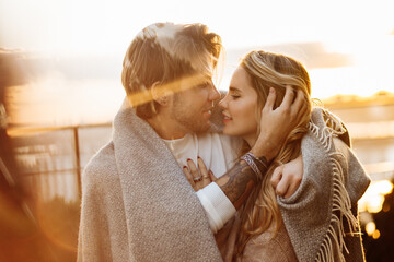 portrait of happy beautiful couple at the sunset, cuddling in cozy blanket. charming loving blond ma
