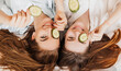 © Daria Lukoiko - Two girls make homemade face and hair beauty masks. Cucumbers for the freshness of the skin around the eyes. Women take care of youthful skin. Girlfriends laugh at home lying on the floor on pillows.