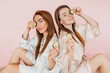 © Daria Lukoiko - Two girls make homemade face beauty masks. Cucumbers for the freshness of the skin around the eyes. Women take care of youthful skin. Girlfriends laughing and having fun in spa on pink background