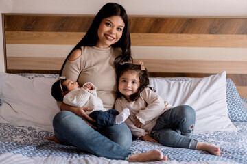 Hispanic young mom hugging her daughters in bed. Happy loving family, small family home portrait.