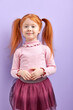 © alfa27 - Shy diligent redhead child girl with two ponytails posing at camera, smiling, incredible girl in skirt isolated on purple studio background