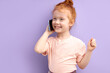 © alfa27 - Redhead child girl communicates on mobile phone, smiles and talks isolated on purple background. Closeup smiling kid talking on smartphone. People sincere emotions lifestyle concept