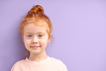 cute smiling caucasian child girl with red hair and big blue eyes isolated over purple background. natural red haired girl with freckles look at camera with pleasant face, glad and nice girl