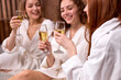 © alfa27 - young women in white bathrobe relaxing in spa salon, drinking champagne, clinking glasses, celebrating holidays together. beauty, people concept. focus on hands with beverage