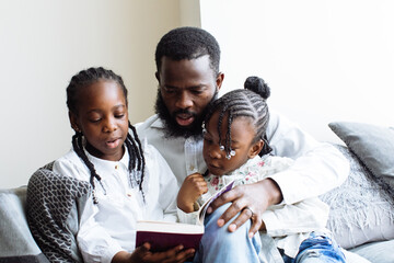 Wall Mural - Father reads a book to his two daughters on sofa