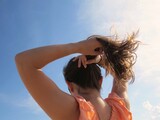 Fototapeta  - Woman putting her hair into a ponytail on a sunny day