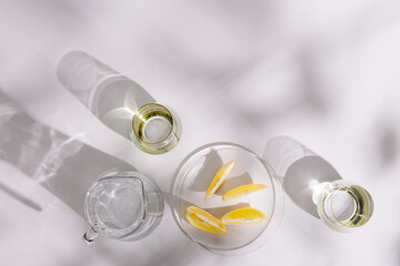 Life style photo with glass cups and jug with fresh water and plate with citrus of lemon on white background. Summer minimal flat lay with hard shadows.