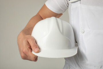 A man in a white work uniform holds a white helmet in his hands. Mock-up.