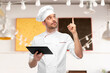 cooking, culinary and people concept - male chef in toque with tablet pc computer pointing finger up over restaurant background