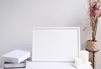 Mock up white poster frame,candles,book  and beautiful dried flowers in modern wood vase  composition over white wooden table room interior