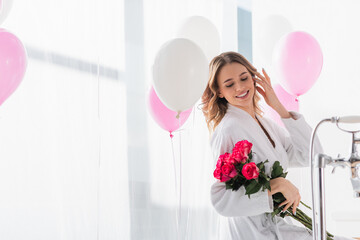 Wall Mural - Cheerful woman holding roses near balloons in bathroom