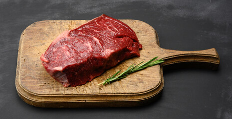 Wall Mural - raw piece of beef steak lies on an old brown wooden cutting boar