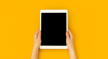 Woman hand holds digital tablet mockup with blank screen, education and application concept template, bright yellow background, top view and copy space photo